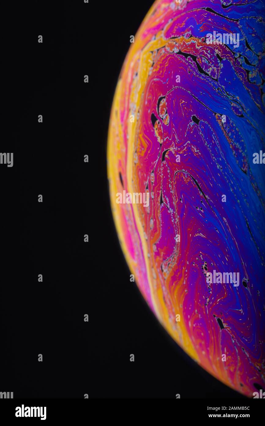Gros plan sur l'arc-en-ciel psychédélique de couleurs mélangeant et tourbillonnant dans une bulle de savon pour ressembler à une galaxie ou une planète fantasy isolé un fond noir Banque D'Images