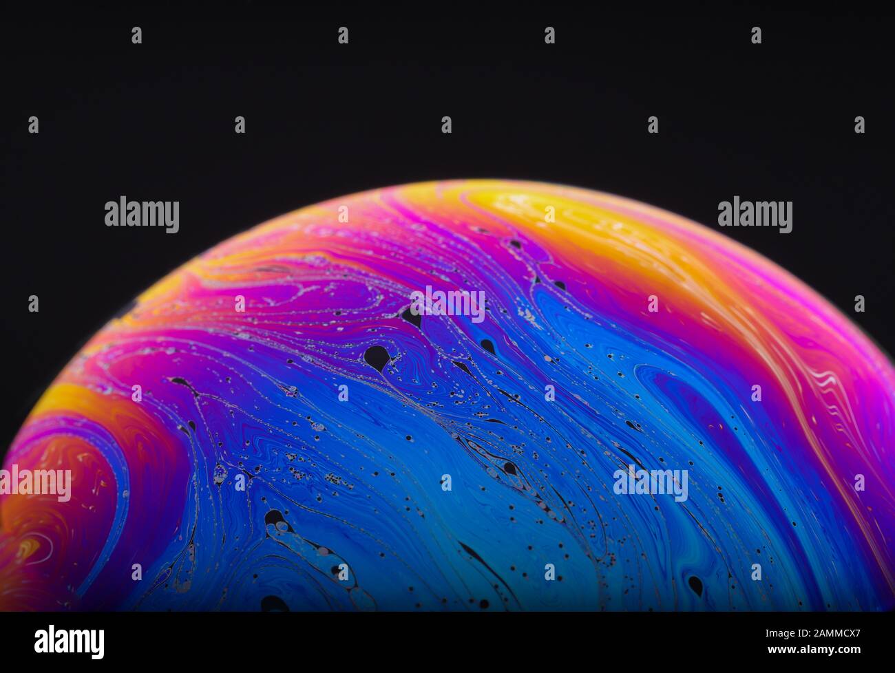 Gros plan sur l'arc-en-ciel psychédélique de couleurs mélangeant et tourbillonnant dans une bulle de savon pour ressembler à une galaxie ou une planète fantasy isolé un fond noir Banque D'Images