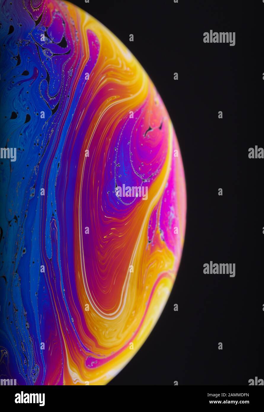 Gros plan sur l'arc-en-ciel psychédélique de couleurs mélangeant et tourbillonnant dans une bulle de savon pour ressembler à une galaxie ou une planète fantasy isolé un fond noir Banque D'Images