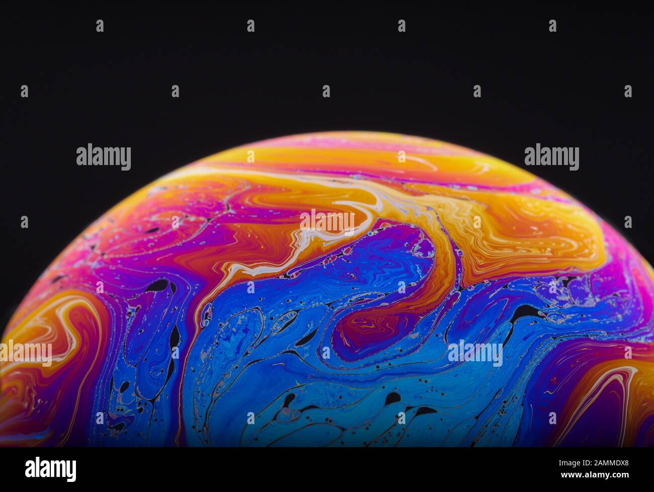Gros plan sur l'arc-en-ciel psychédélique de couleurs mélangeant et tourbillonnant dans une bulle de savon pour ressembler à une galaxie ou une planète fantasy isolé un fond noir Banque D'Images