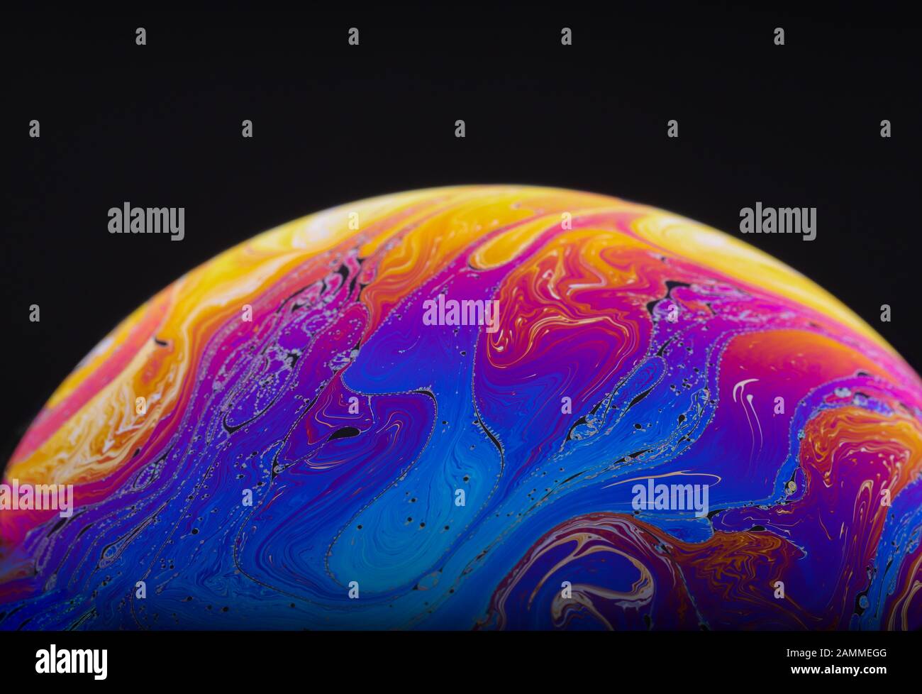 Gros plan sur l'arc-en-ciel psychédélique de couleurs mélangeant et tourbillonnant dans une bulle de savon pour ressembler à une galaxie ou une planète fantasy isolé un fond noir Banque D'Images