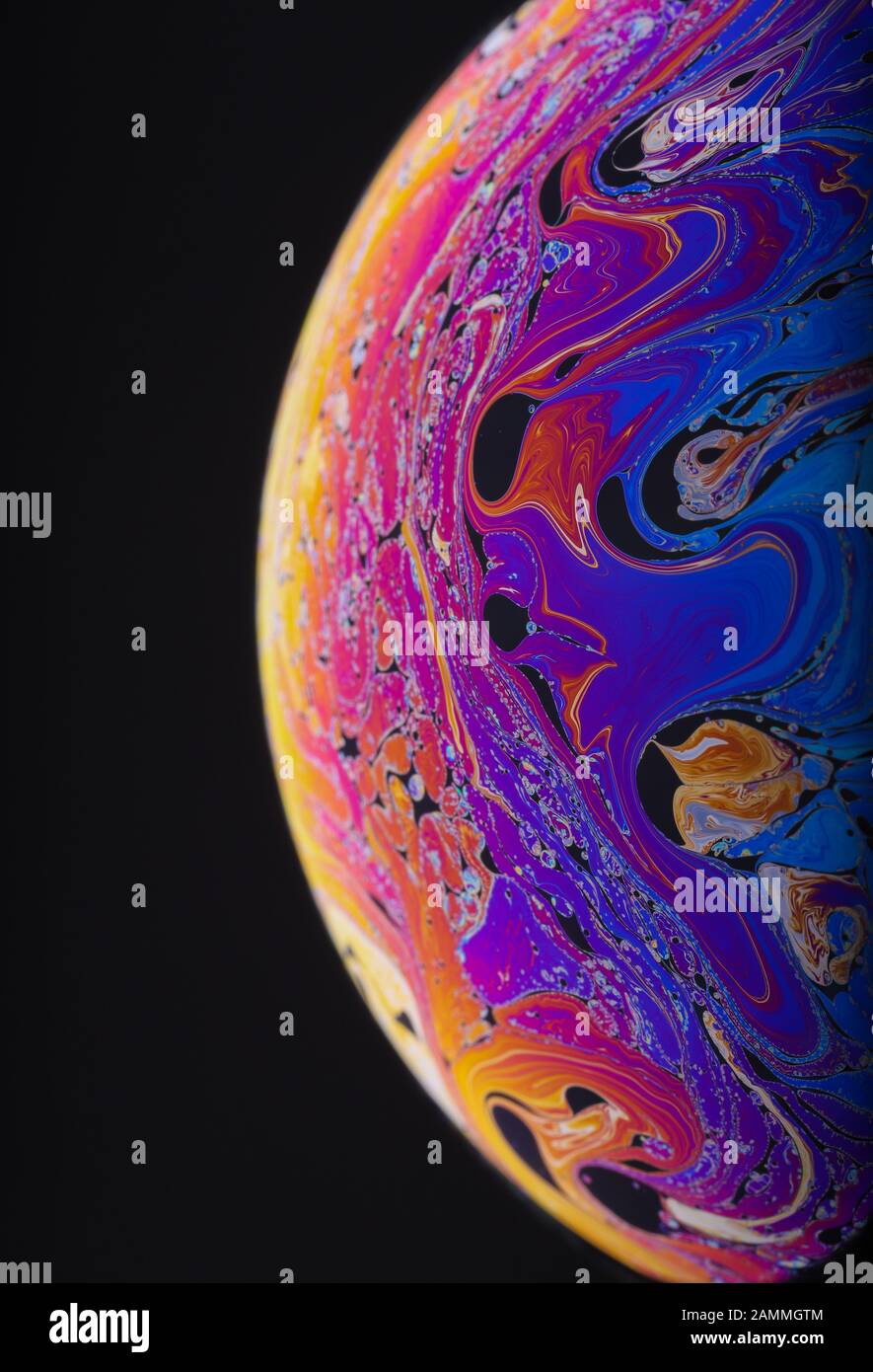 Gros plan sur l'arc-en-ciel psychédélique de couleurs mélangeant et tourbillonnant dans une bulle de savon pour ressembler à une galaxie ou une planète fantasy isolé un fond noir Banque D'Images
