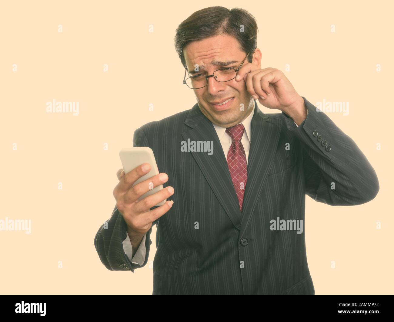 Studio tourné de jeune homme d'affaires persan utilisant le téléphone mobile tout en pleurant Banque D'Images