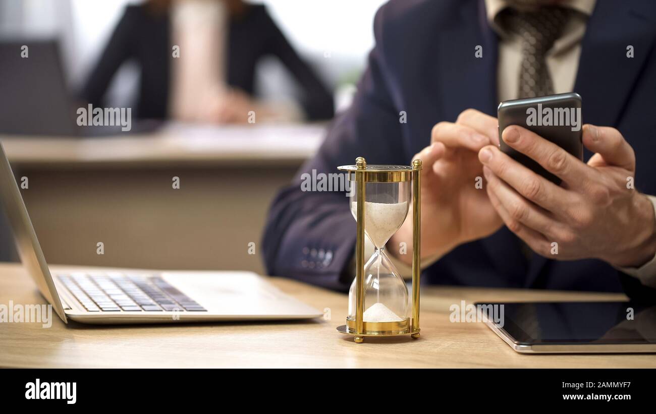 HourGlass mesure du temps, homme d'affaires utilisant le téléphone mobile, procrastination Banque D'Images