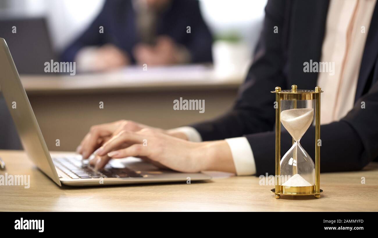 Femme travaillant sur un ordinateur portable au bureau, sablier mesurant le temps, l'efficacité au travail Banque D'Images