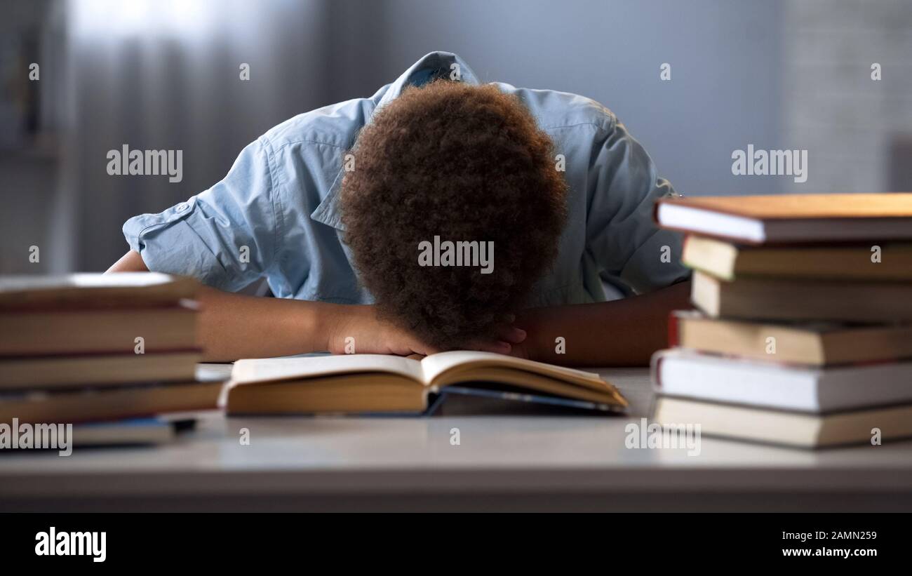 Enfant de sexe masculin dormant sur la table fatigué des livres de lecture, faisant beaucoup de devoirs Banque D'Images