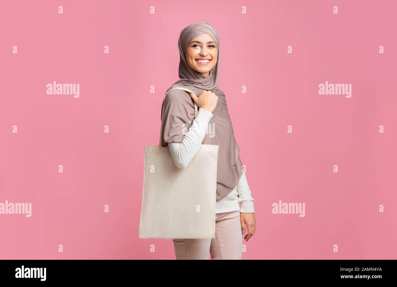 Une femme islamique gaie dans un foulard se posant avec un sac à provisions fourre-tout ECO Banque D'Images