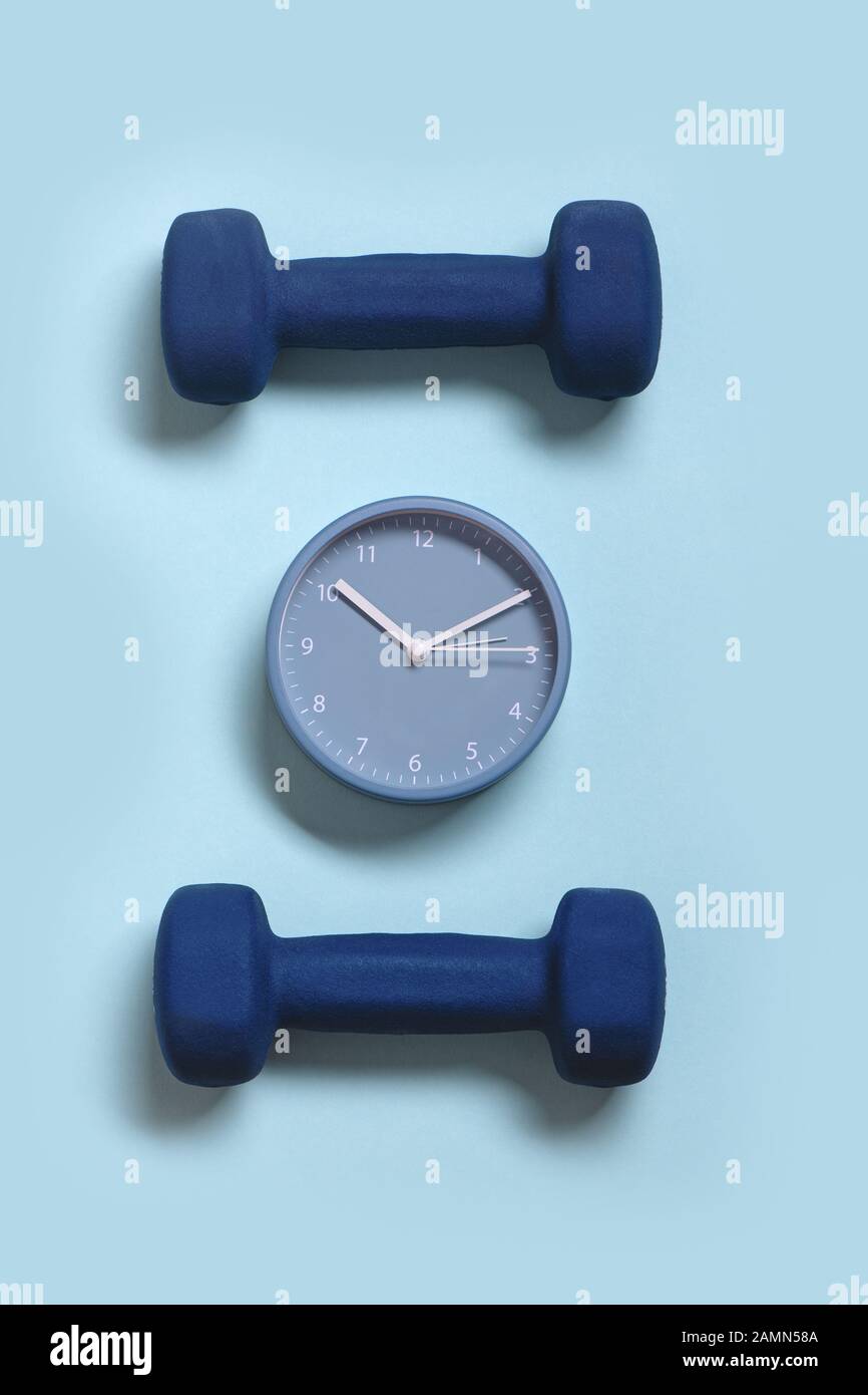 Horloge et paire de haltères sur fond bleu pastel. Concept de temps pour le sport. Banque D'Images