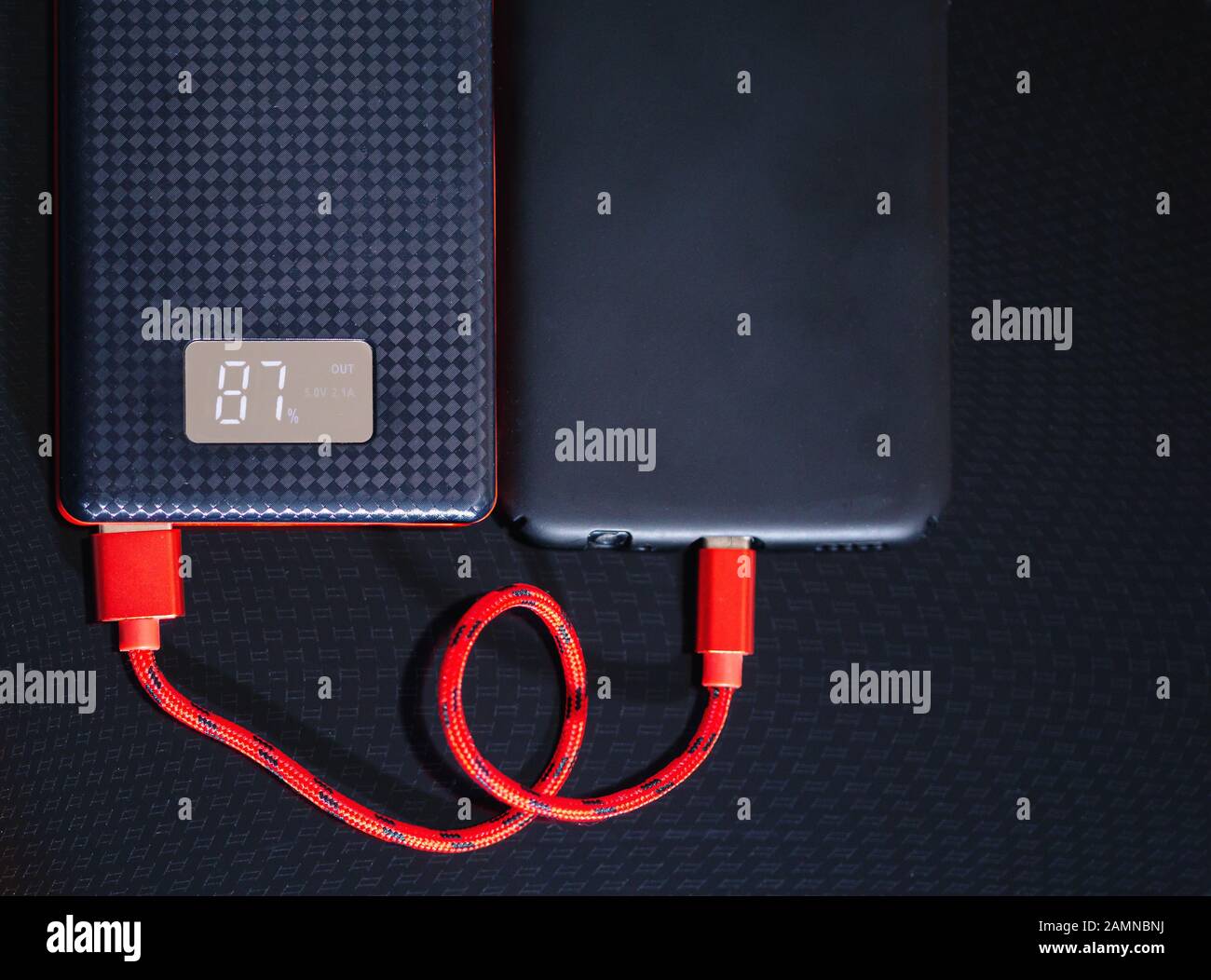 Chargement du smartphone avec la Power Bank noire via un câble USB sur fond noir. Vue de dessus. Banque D'Images Chargement du smartphone avec la Power Bank noire via un câble USB sur fond noir. Vue de dessus. Banque D'Images