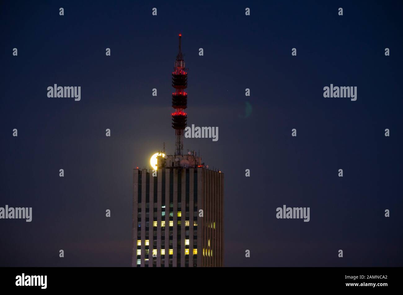 Pleine lune dans la ville. Grand bâtiment avec une antenne spire Banque D'Images