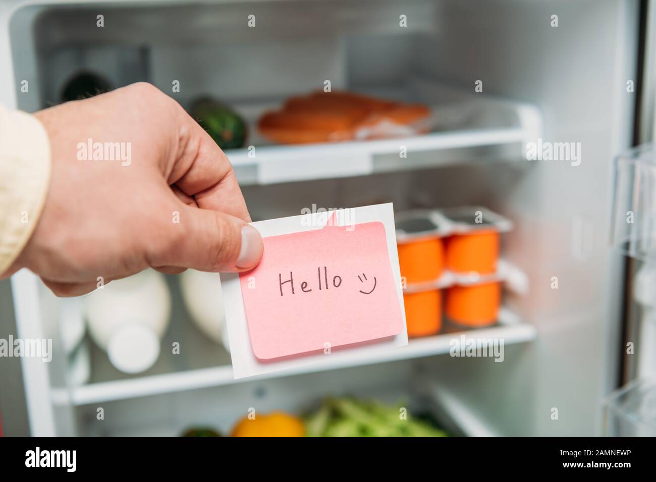 vue courte de l'homme tenant un pense-bête avec des lettres de bonjour près d'un réfrigérateur ouvert avec des aliments frais sur les étagères Banque D'Images