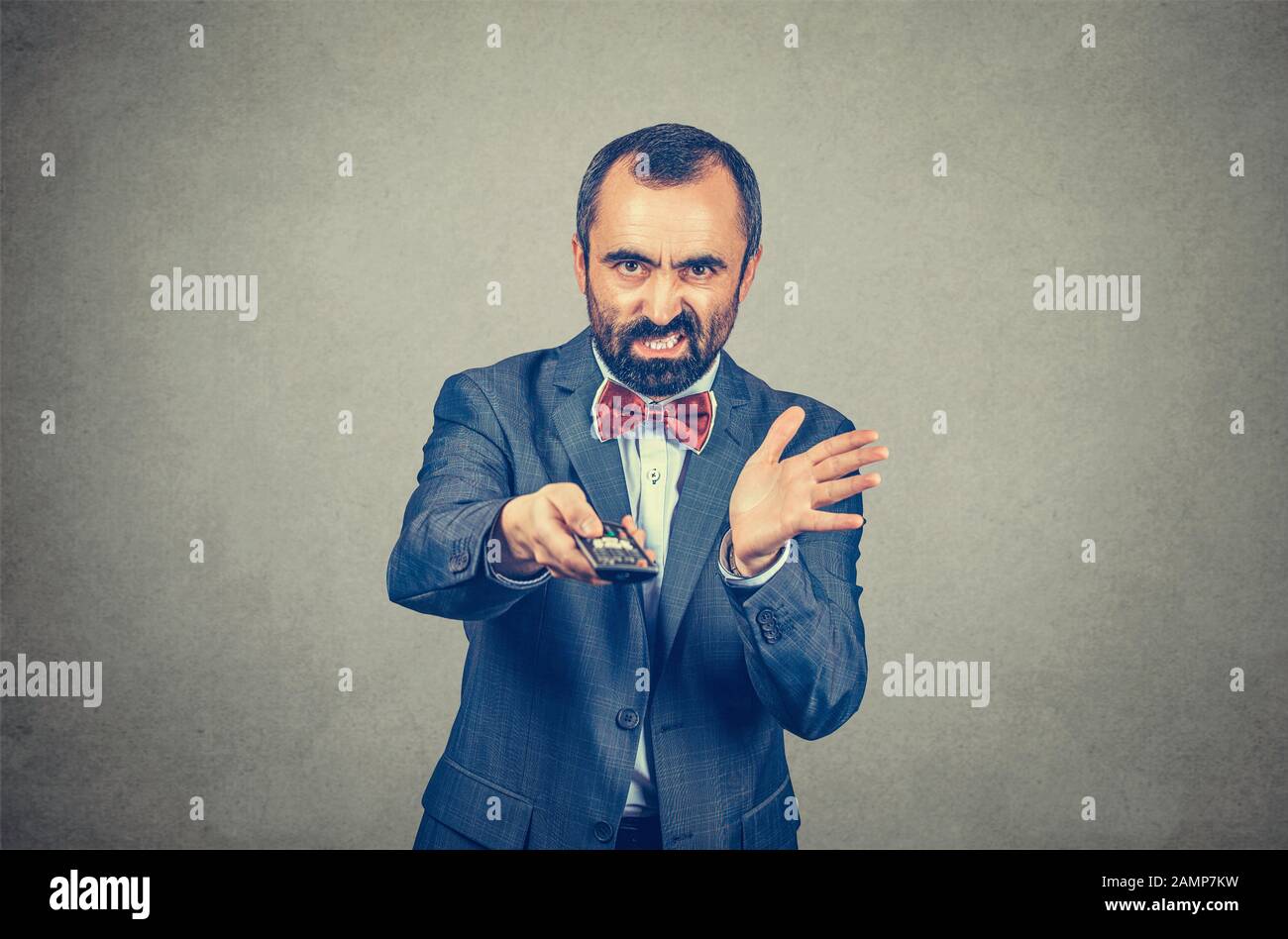 Ennui. Un homme d'âge mûr mécontent et mécontent en colère qui tente de changer de chaîne avec une télécommande de télévision. Modèle mixte barbu isolé sur gris Banque D'Images