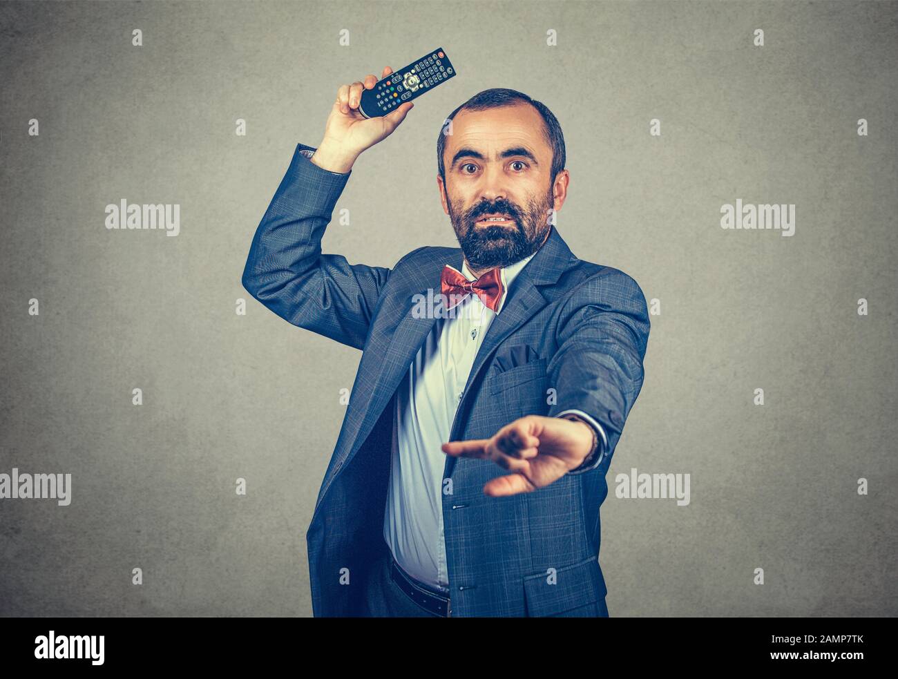 Portrait de demi-longueur de corps d'un homme jetant une télécommande de télévision regardant votre appareil photo peur et fâché. Modèle mixte barbu isolé sur le dos gris Banque D'Images