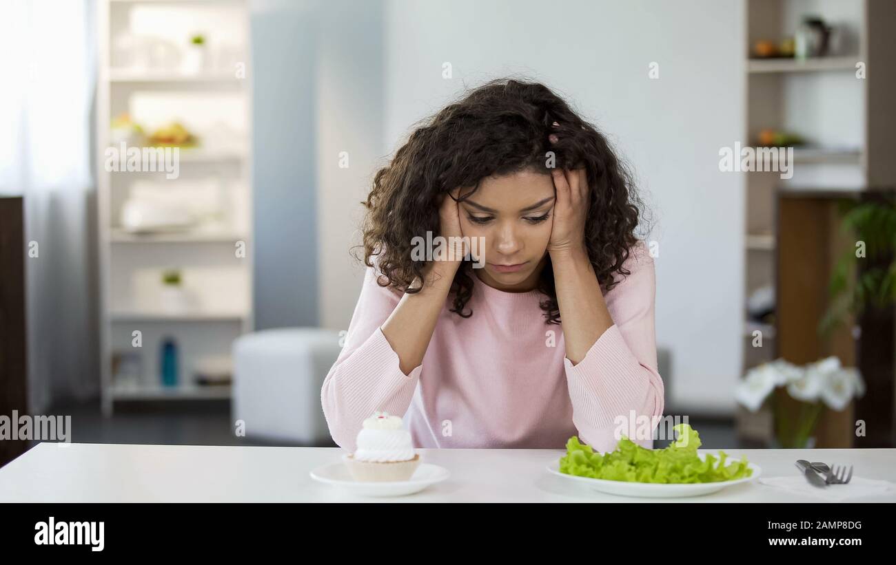 Jeune femme biraciale choisir entre salade et bonbons, choix de soins de santé Banque D'Images