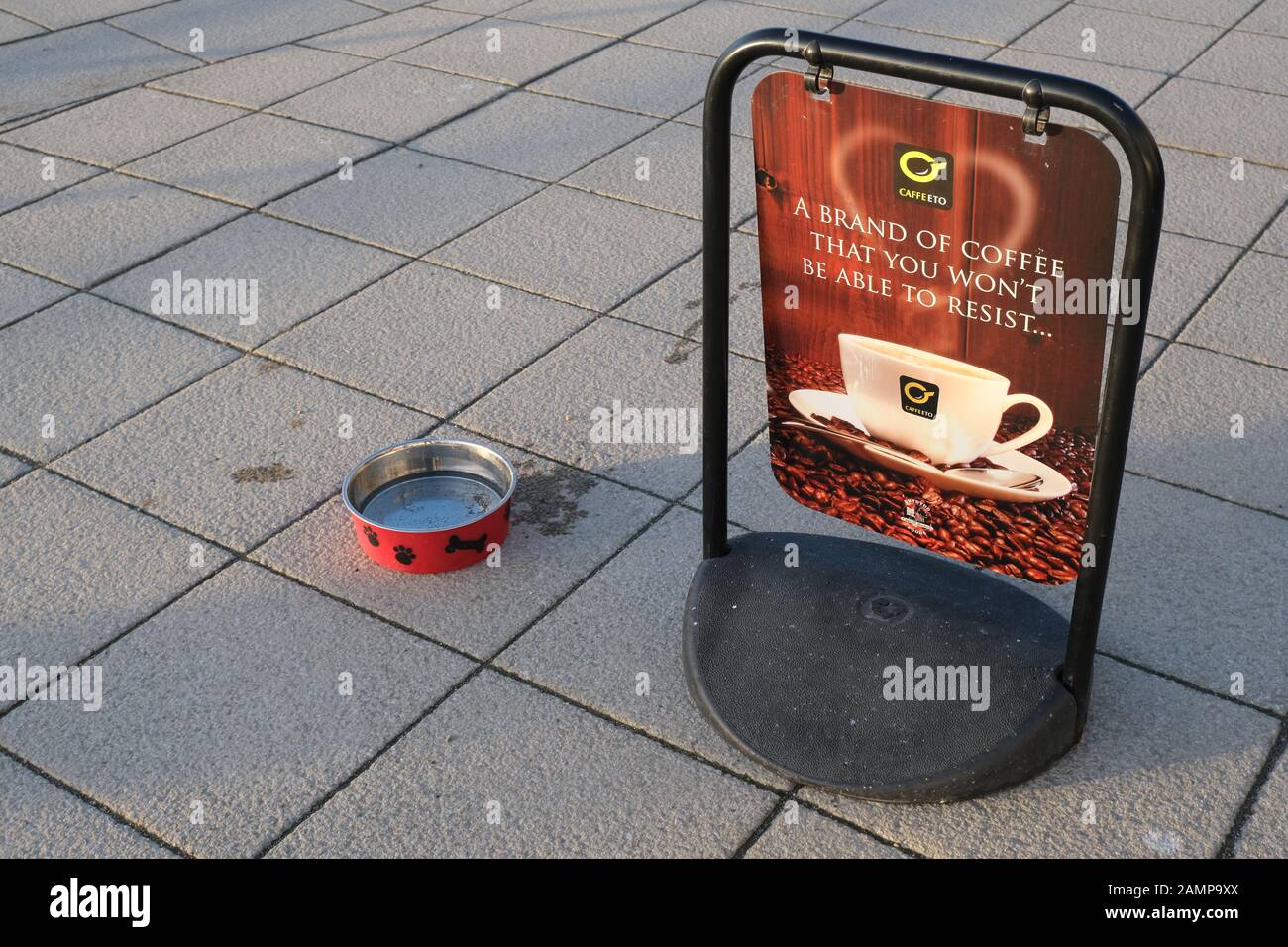 Bol à eau pour chien rouge et café [Caffeeto] panneau pivotant sur un pavé plat carré (trottoir) Banque D'Images