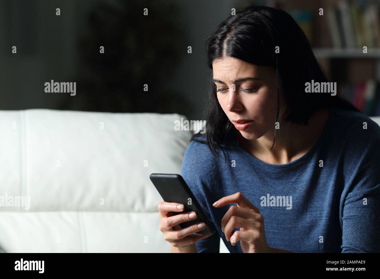 Une femme inquiète à vérifier le texte du téléphone portable assis sur un canapé dans la nuit à la maison dans la nuit Banque D'Images