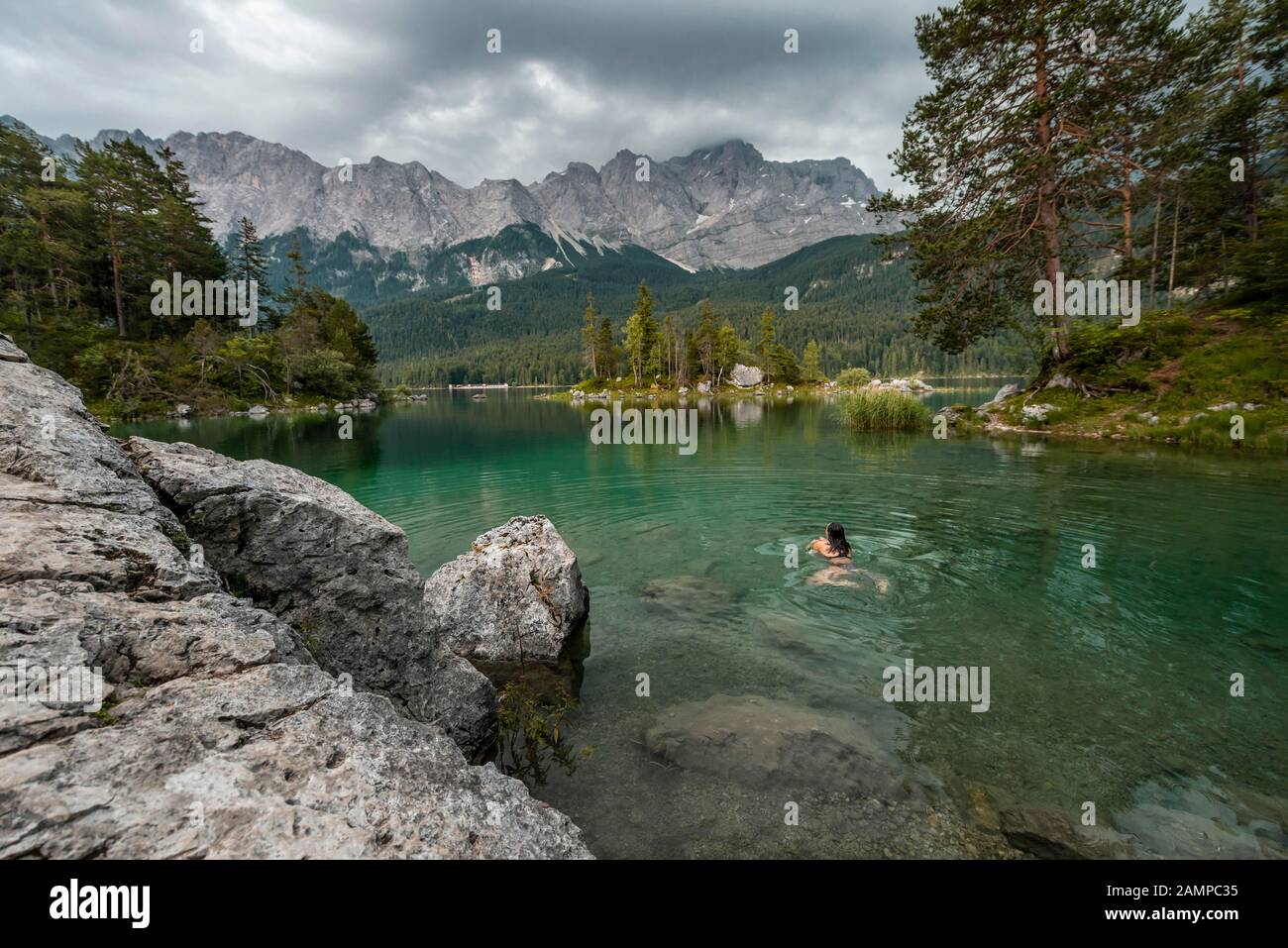 Femme nageant dans le lac, vue sur le lac d'Eibsee en face du massif de Zugspitze avec Zugspitze, nuageux, plage de Wetterstein, près de Grainau, Haute-Bavière Banque D'Images