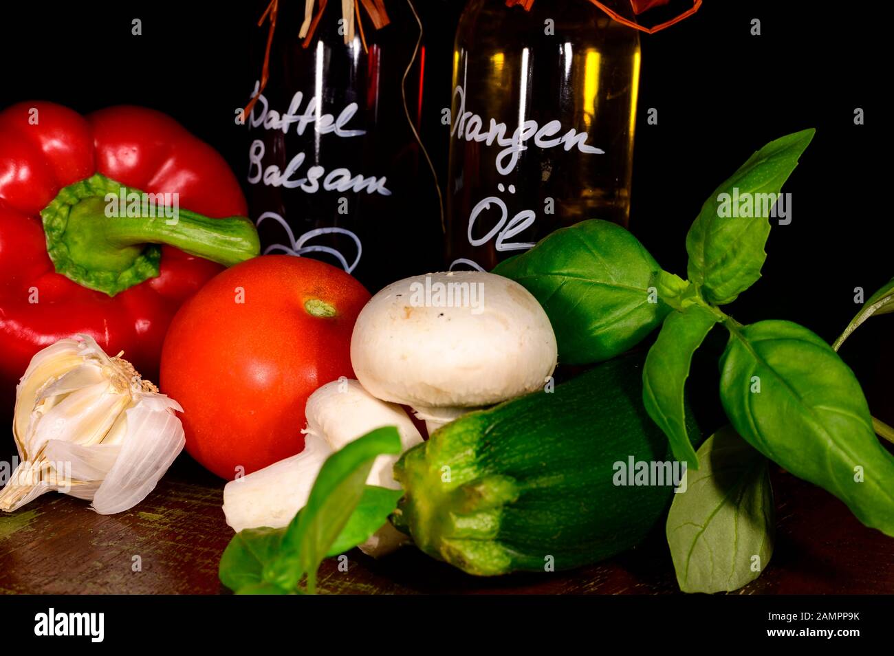 Divers ingrédients frais pour la préparation d'un repas comme le basilic, l'ail et la tomate avec de l'huile balsamique et orange de date en arrière-plan. Banque D'Images