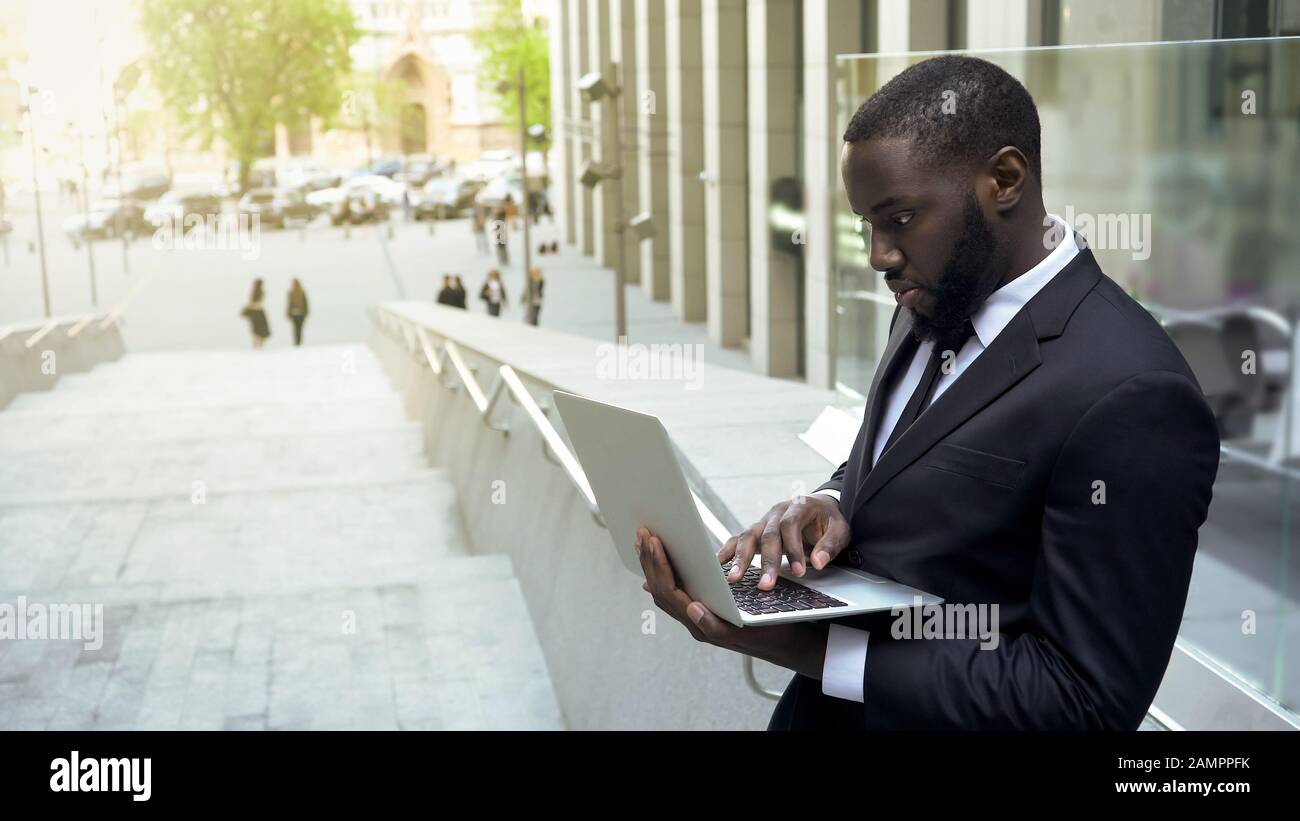 Homme d'affaires noir qui vérifie les fichiers sur l'ordinateur portable, en surtravaillant pendant la pause déjeuner Banque D'Images