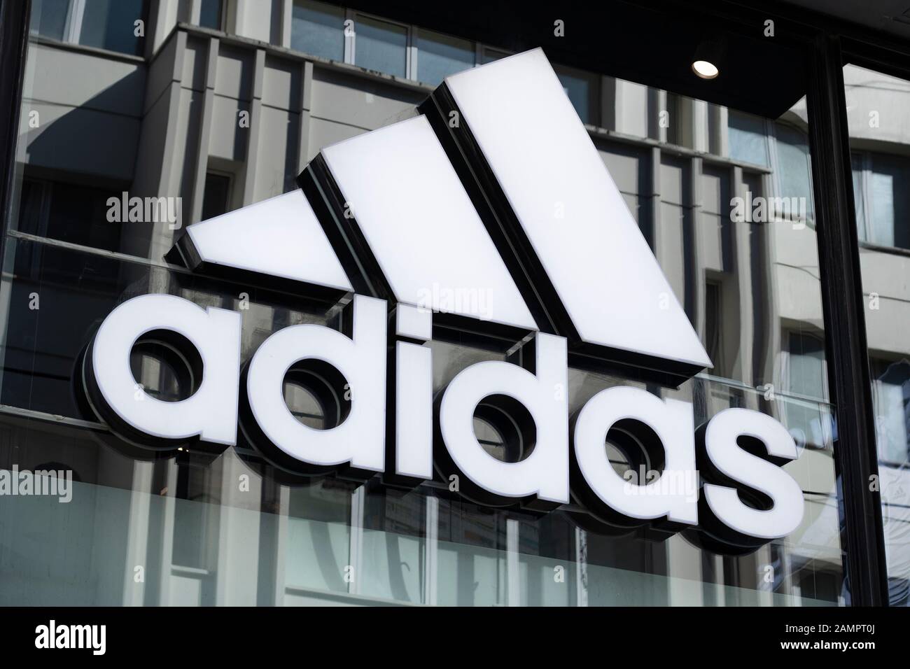 Adidas signe pendu sur le seuil de fenêtre en verre. Gros plan. La photo a  été prise avec contraste. Le tableau écrit le nom et le logo adidas en noir  et blanc