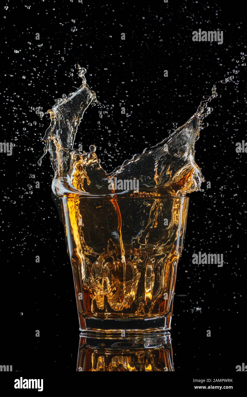 Verre de whisky avec splash isolé sur fond noir Banque D'Images