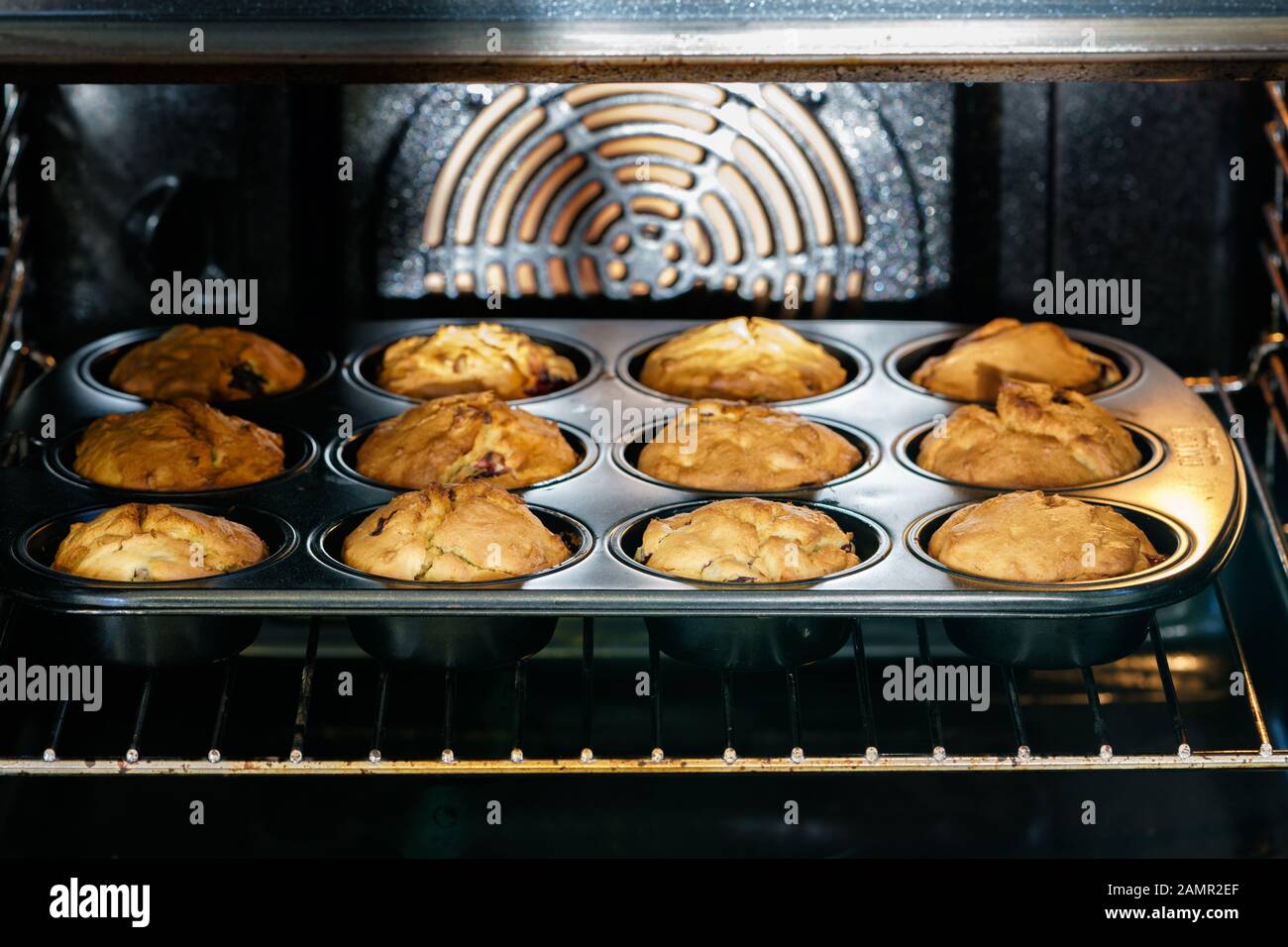Muffins maison aux cerises dorées à la vanille de légumes dans une poêle à muffins noire dans un four éclairé - vue inclinée, format horizontal Banque D'Images