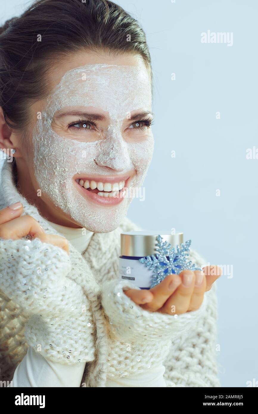 femme moderne souriante dans un sweat-shirt à col roulé et un gilet avec  masque facial blanc montrant un bol cosmétique avec flocons de neige et  isolé sur un concert d'hiver Photo Stock -