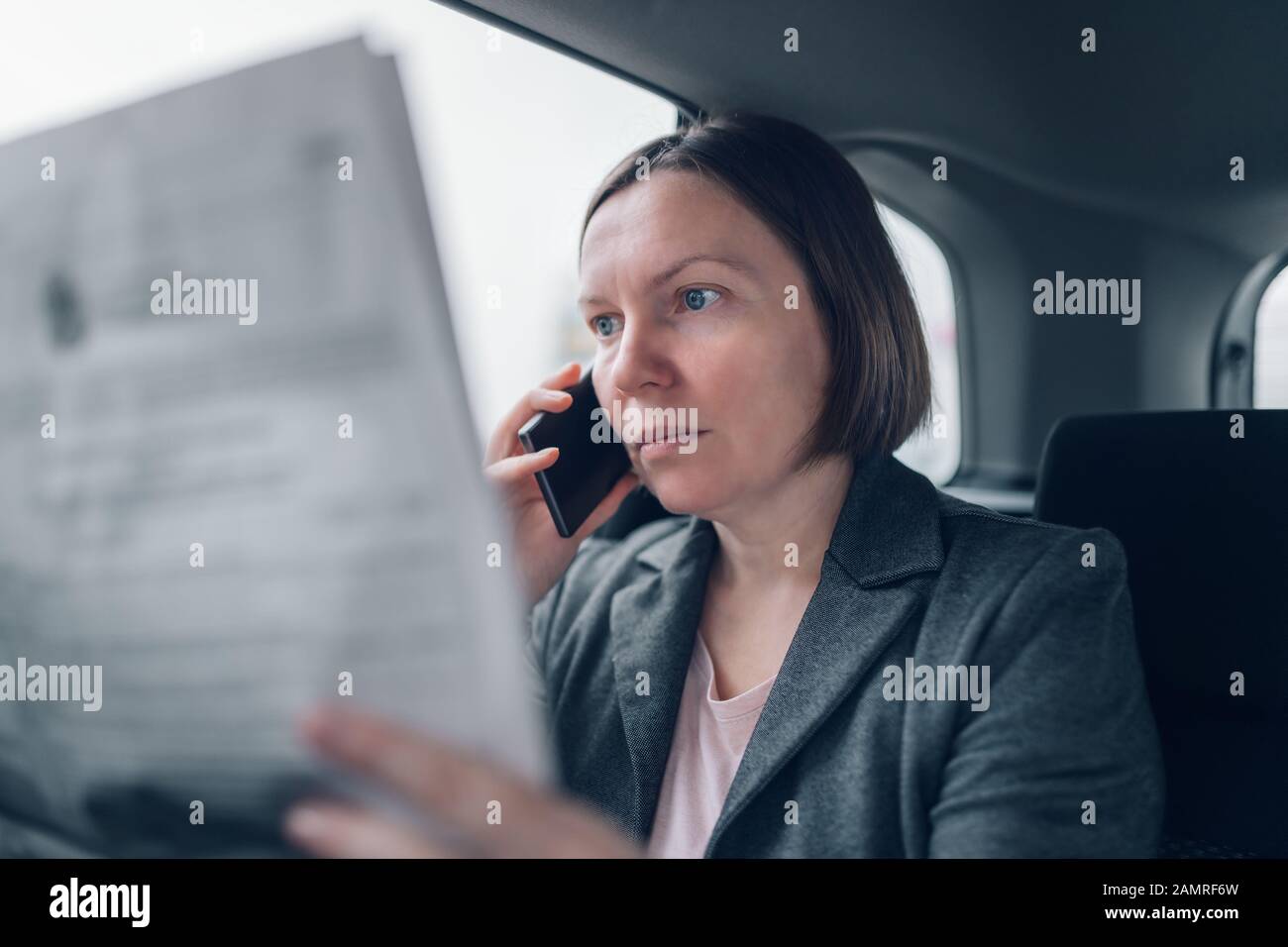 Businesswoman reading newspaper et à l'aide de téléphone mobile à l'arrière de voiture lors des trajets au travail, selective focus Banque D'Images