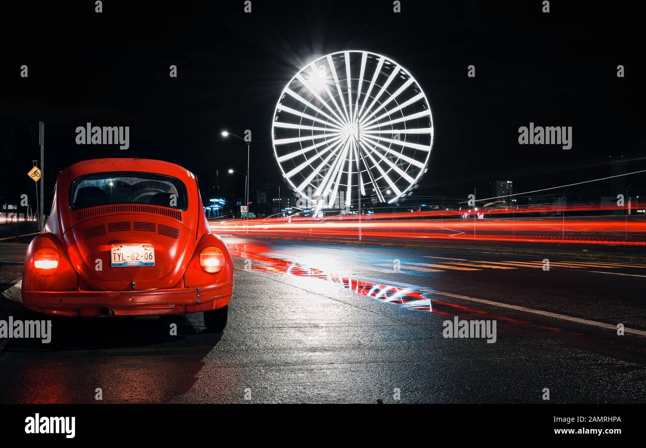 Angélopolis, Puebla de Zaragoza, Mexique, 15 octobre 2018 - photo de rue de la vieille voiture Volkswagen Beetle avec une roue géante de la ville de Puebla la nuit. Longue exposition de la route mexicaine. Banque D'Images