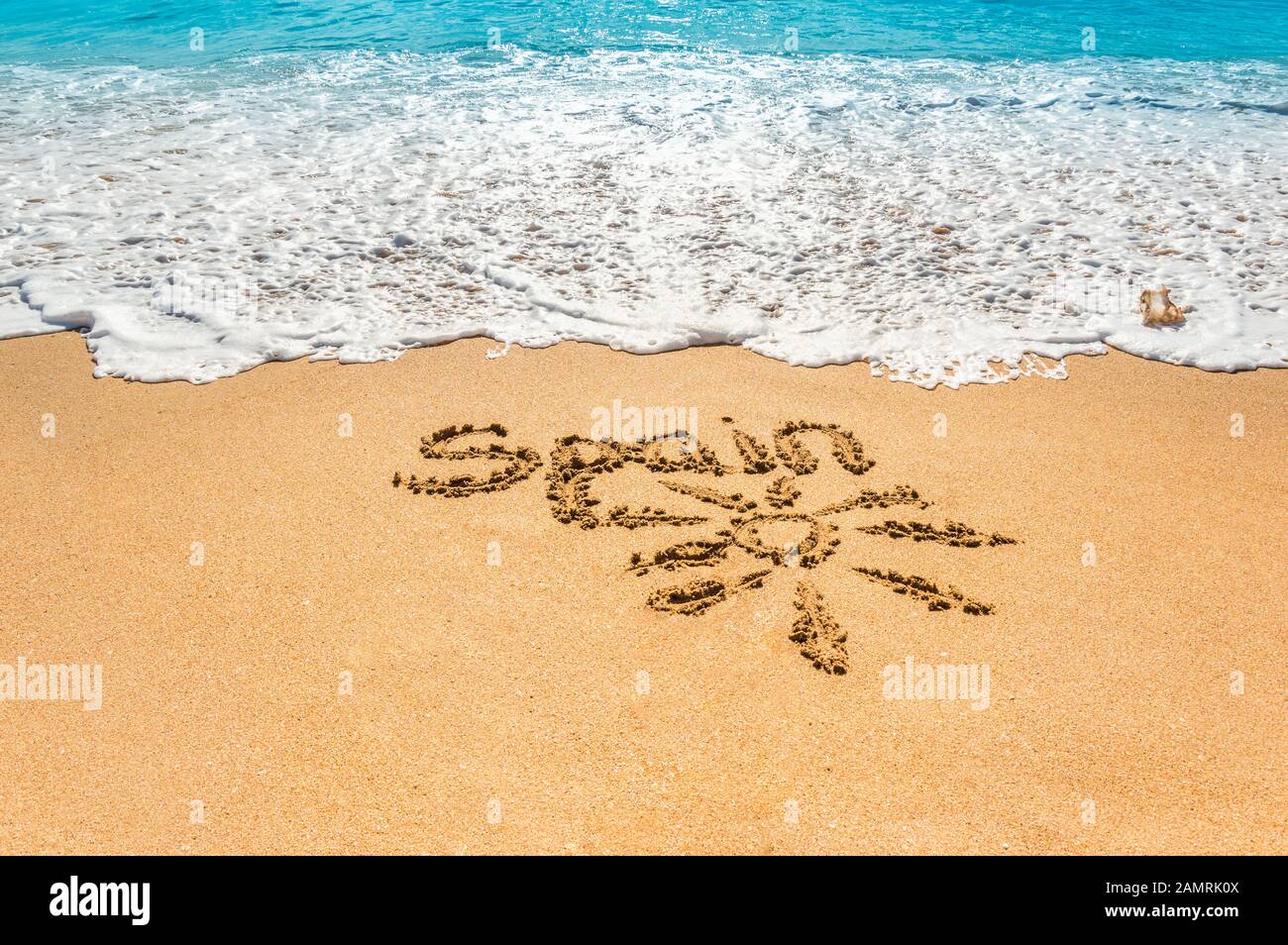 Texte écrit à la main Espagne et symbole du soleil sur la plage de sable doré avec des vagues à venir. Concept de vacances chaudes d'été et de vacances à la mer ou l'océan dans Banque D'Images
