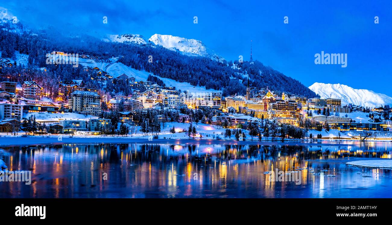 Vue sur les magnifiques lumières nocturnes de la ville de Saint-Moritz en Suisse la nuit en hiver, avec réflexion du lac et des montagnes de neige dans le backgrouind Banque D'Images