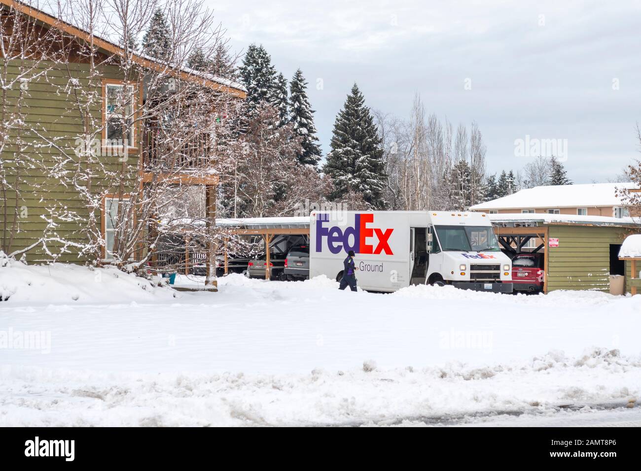 Un chauffeur de FedEx traverse de la neige épaisse jusqu'à son camion après avoir livrer des colis à un appartement en hiver. Banque D'Images