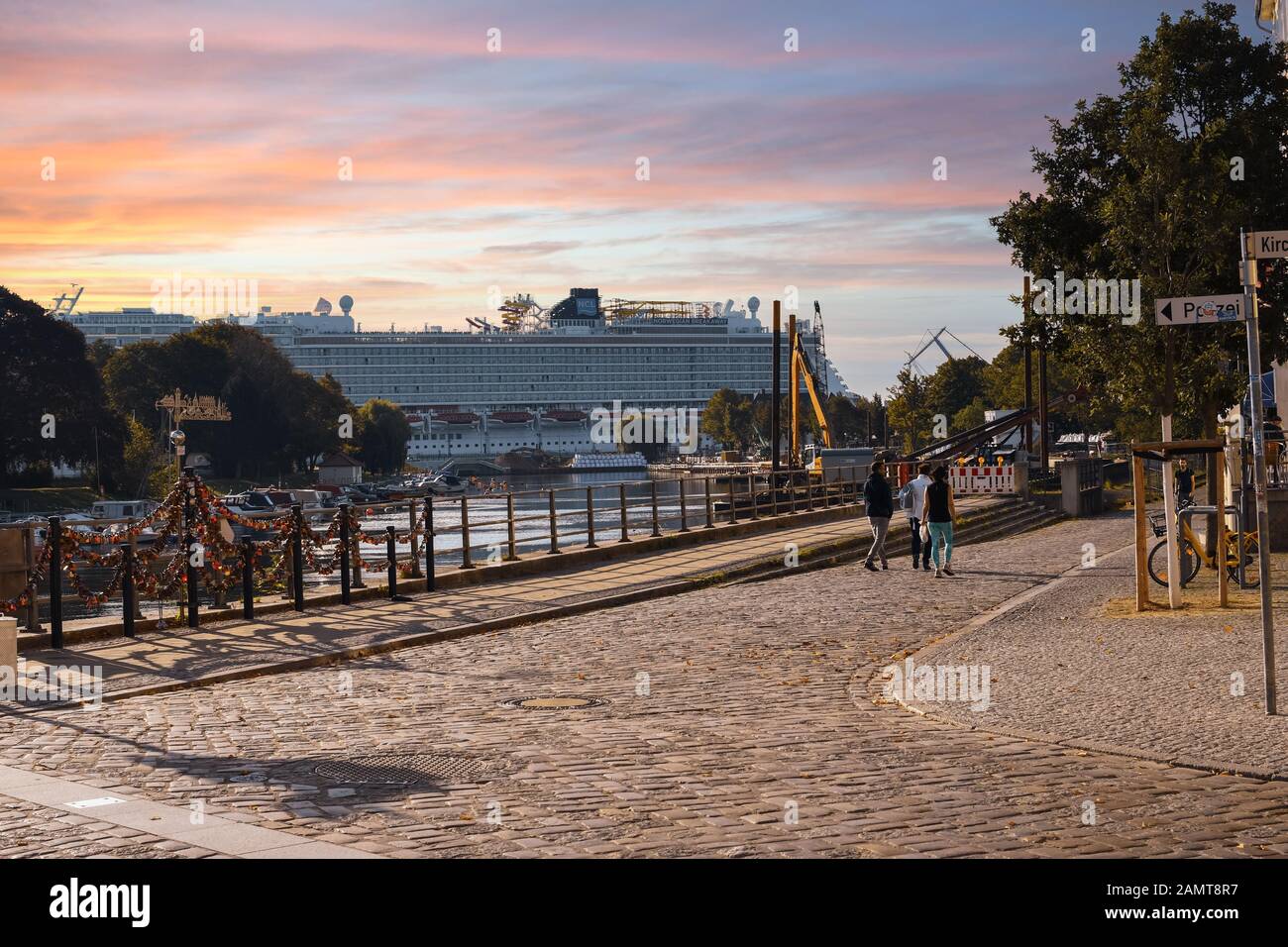 Un bateau de croisière se trouve au port de la ville côtière Baltique de Warnemunde Rostock, en Allemagne, tandis que le soleil se couche sous un ciel coloré et les touristes se promenent à pied Banque D'Images