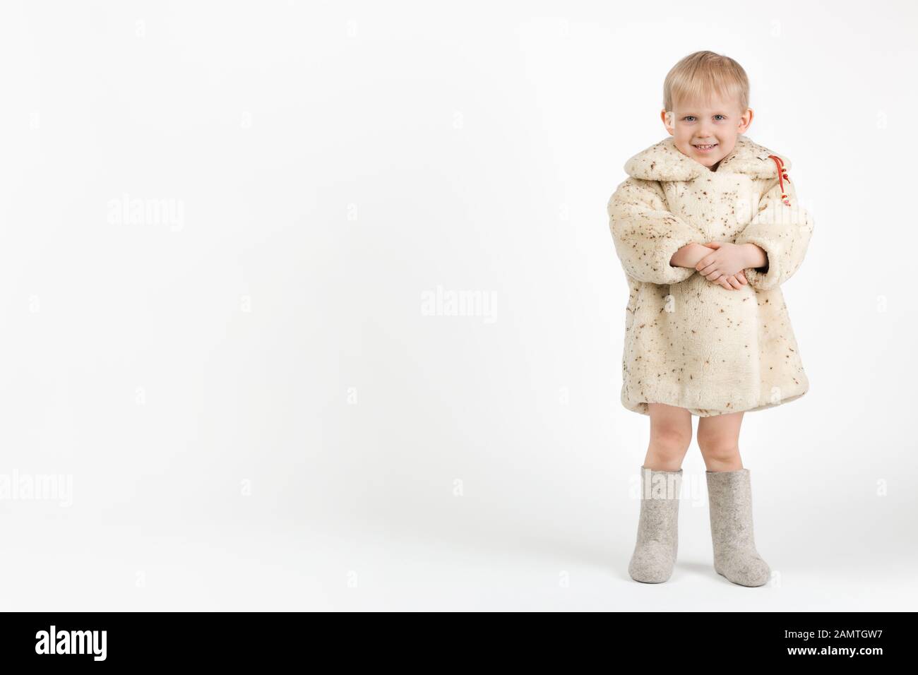 Un enfant tout-petit dans un pelage de mouton ou de peau de mouton soviétique et des bottes de feutre gris sur un fond blanc avec un endroit pour le texte. Un concept pour les sujets sur Rus Banque D'Images