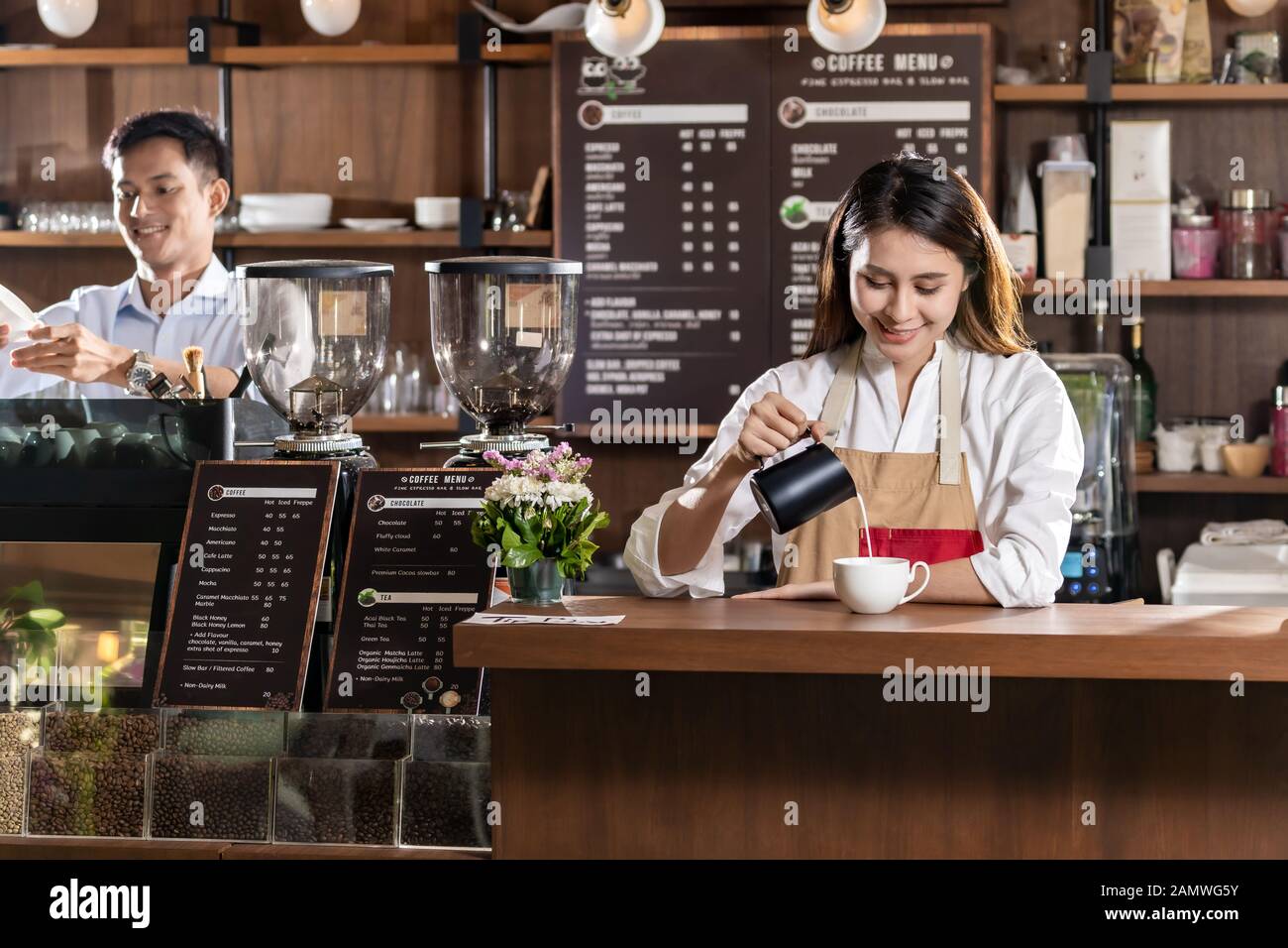Young adult asian female barista pouring lait frais pour préparer du café latte pour client dans un café-bar. Banque D'Images