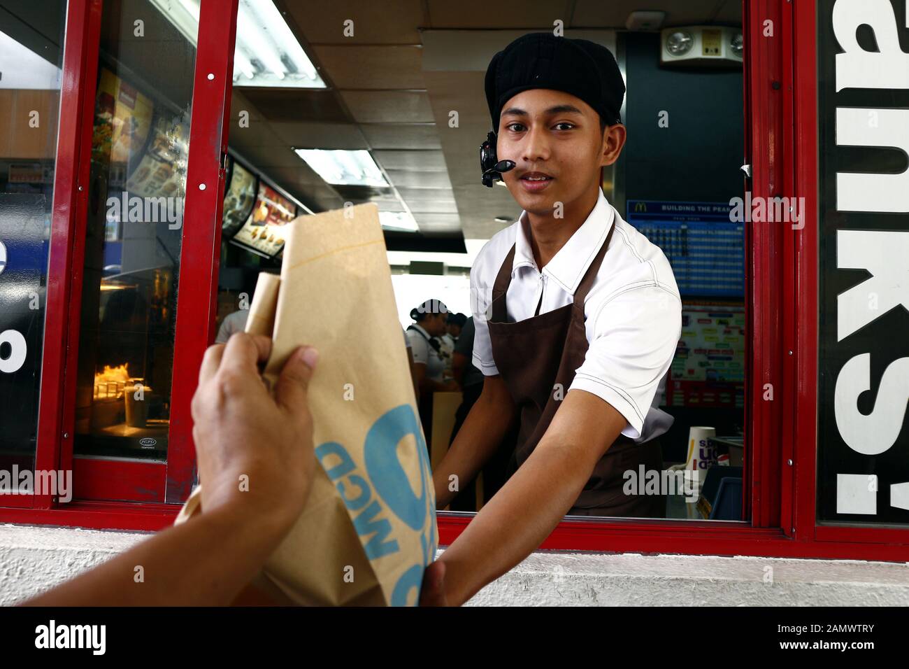 Antipolo City, Philippines - Le 11 janvier 2020 : le travailleur à un fast-food donne la commande de nourriture d'un client à un drive thru fenêtre. Banque D'Images