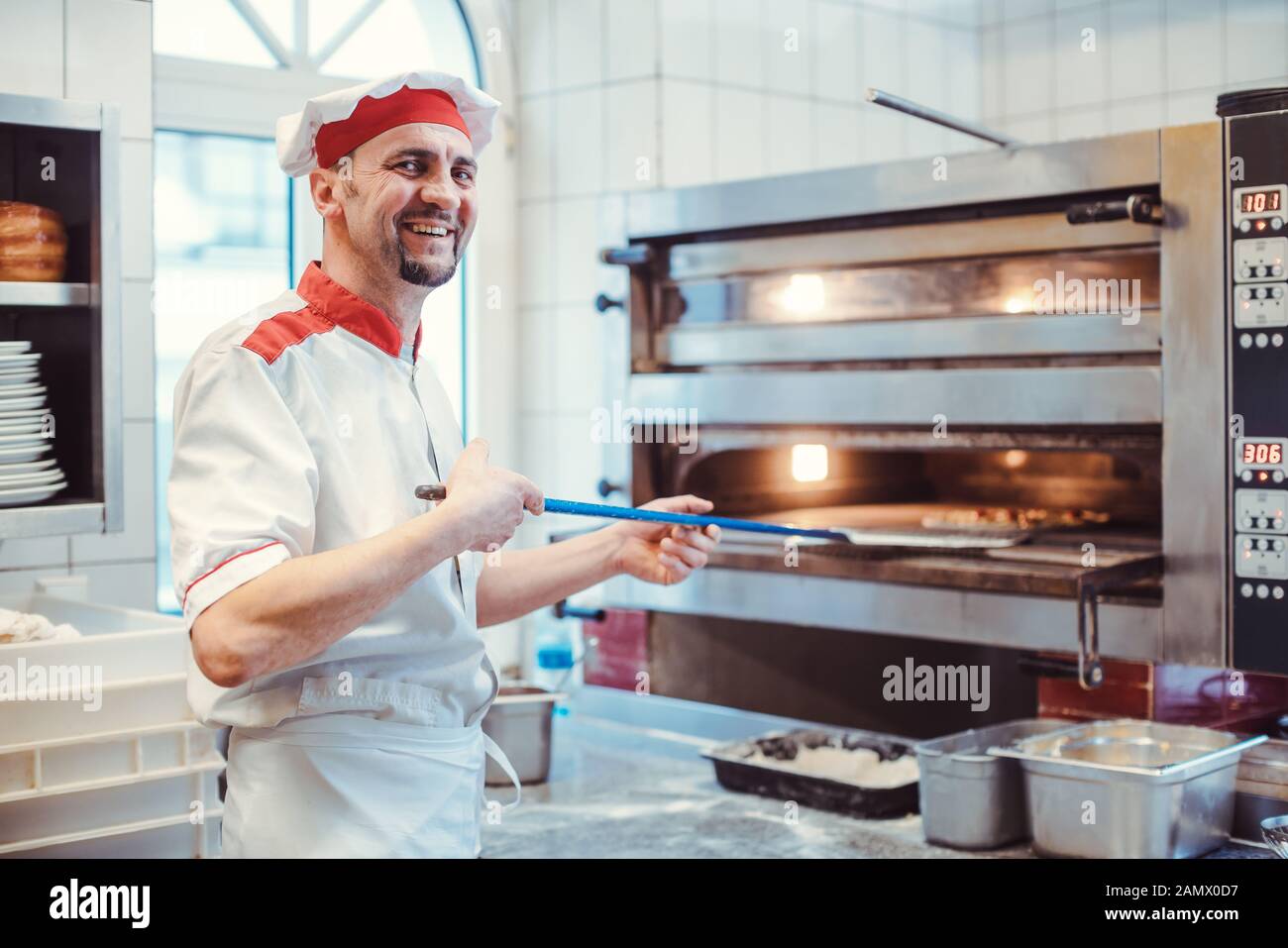 Chef souriant mettant des pizzas au four dans une cuisine de restaurant Banque D'Images