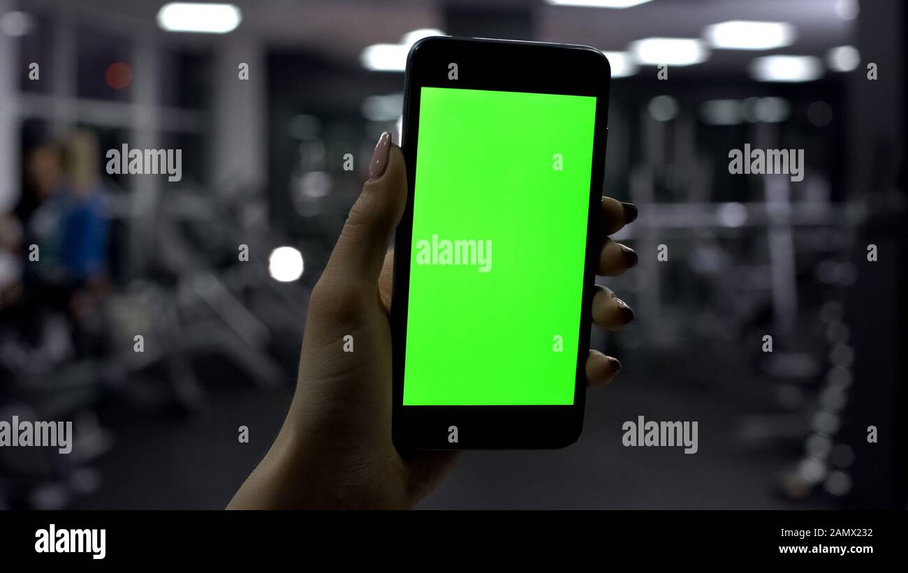 Main féminine tenant smartphone dans la salle de sport, écran vert, application de fitness en ligne Banque D'Images
