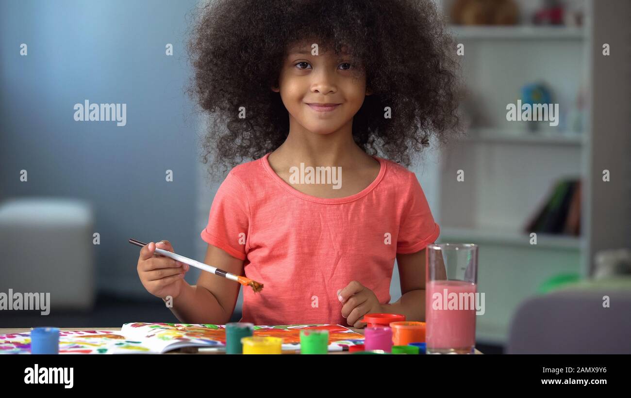 Jolie fille africaine peint une photo et sourire dans l'appareil photo, l'enfance Banque D'Images