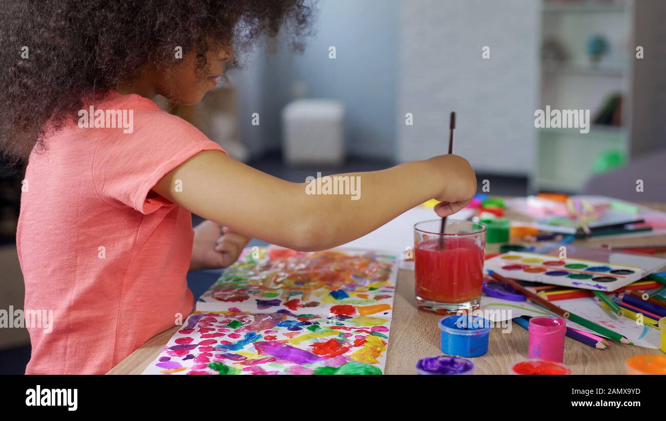 Mignonne fille afro-africaine mettant le pinceau dans l'eau, temps de loisirs Banque D'Images
