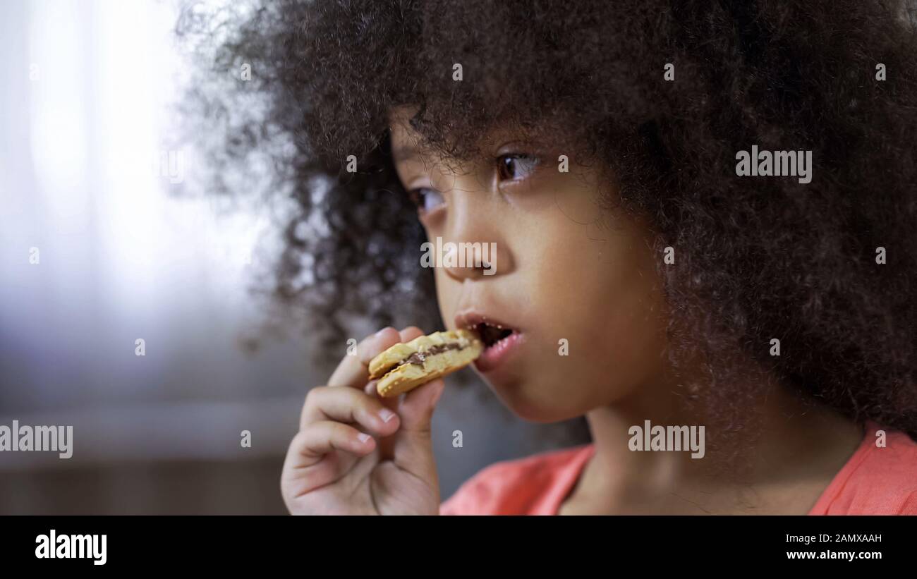 Adorable jeune fille africaine d'âge préscolaire mangeant un cookie sucré avec un gros plan de l'appétit Banque D'Images
