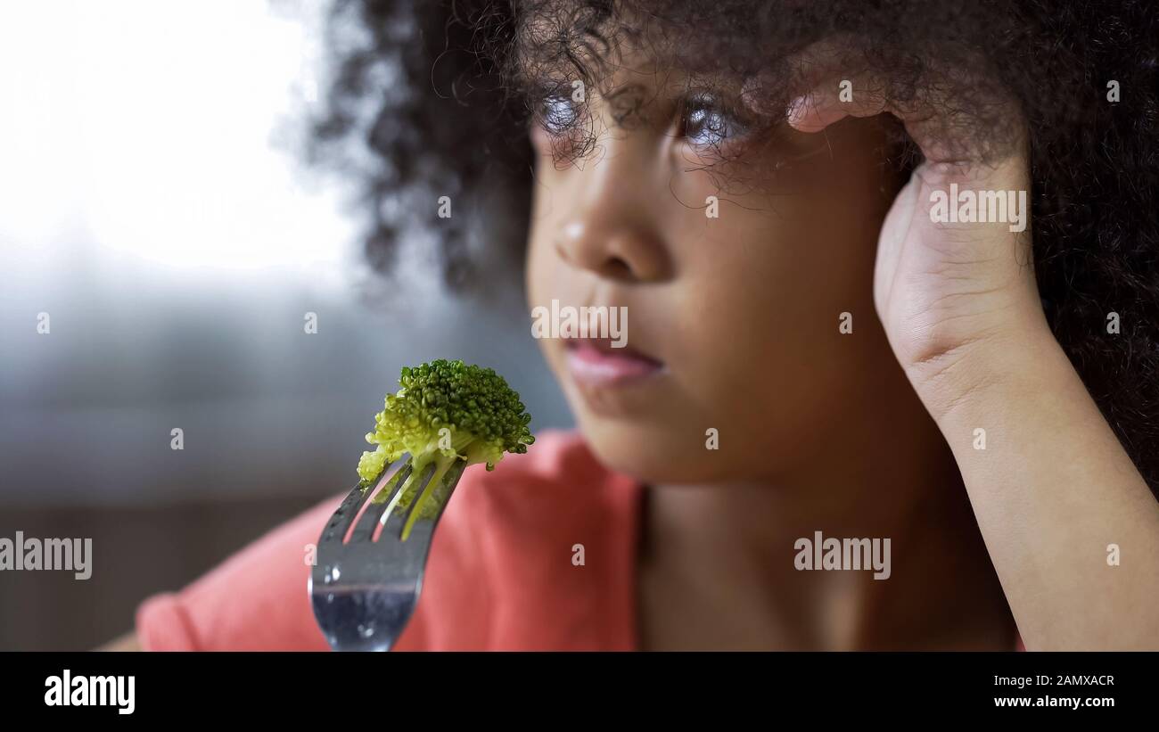 Jolie fille palatto tenant la fourchette avec un morceau de brocoli sur, nourriture sans appétissant Banque D'Images