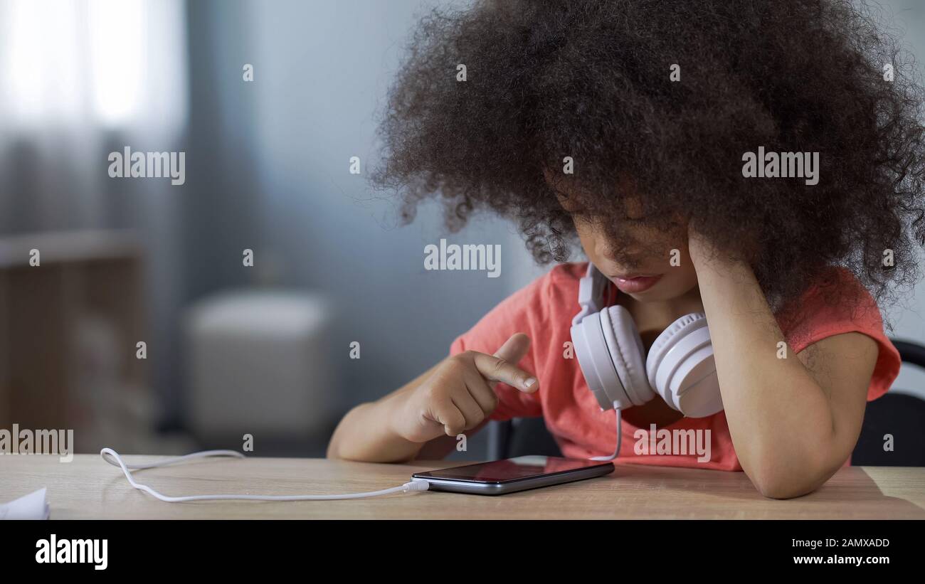 Jeune fille molatto d'âge préscolaire regardant le film sur smartphone seul gadget addiction Banque D'Images