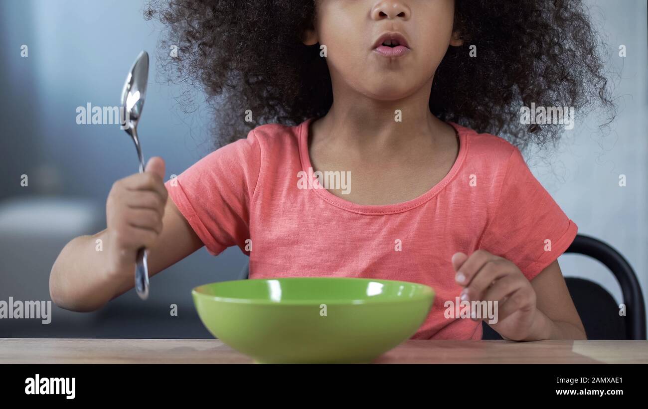 Une jeune fille palatto d'âge préscolaire qui demande le dîner, assise à table avec cuillère Banque D'Images