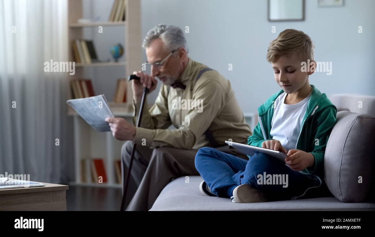 Grandpa lecture de la presse, garçon utilisant la tablette, les générations et le progrès technologique Banque D'Images