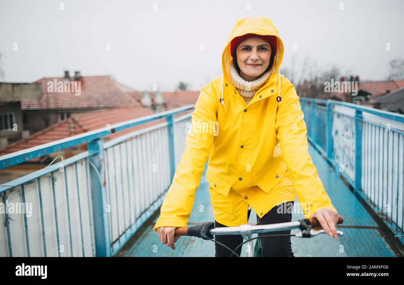 Femme à vélo dans la pluie. Fille en imperméable jaune vélo Banque D'Images