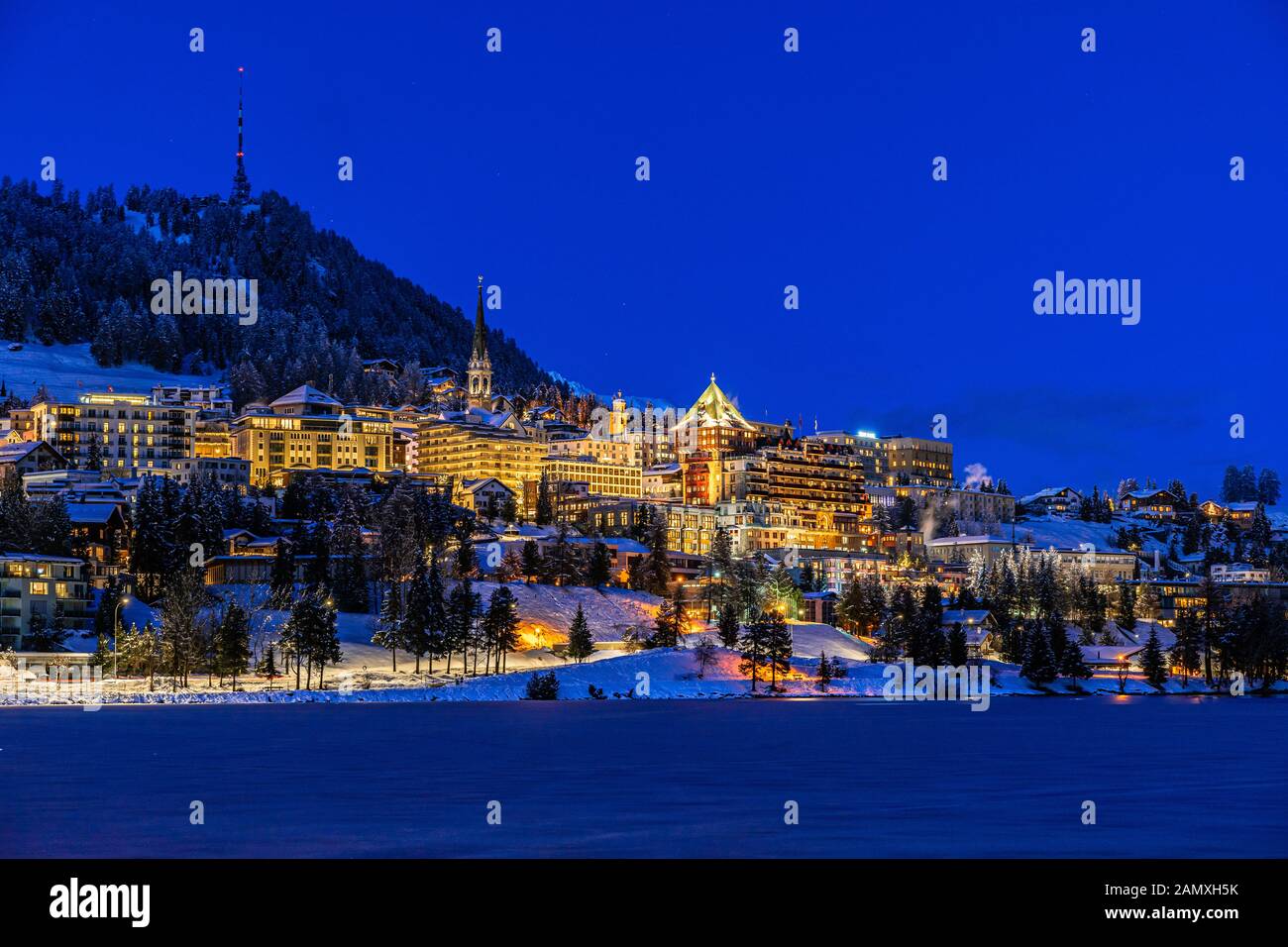 Vue sur les magnifiques lumières nocturnes de la ville de Saint-Moritz en Suisse la nuit en hiver, avec réflexion du lac et des montagnes de neige dans le backgrouind Banque D'Images