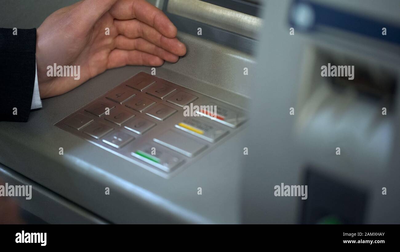 Homme masquant le clavier de la machine de caissier automatisée tout en insérant son code PIN Banque D'Images