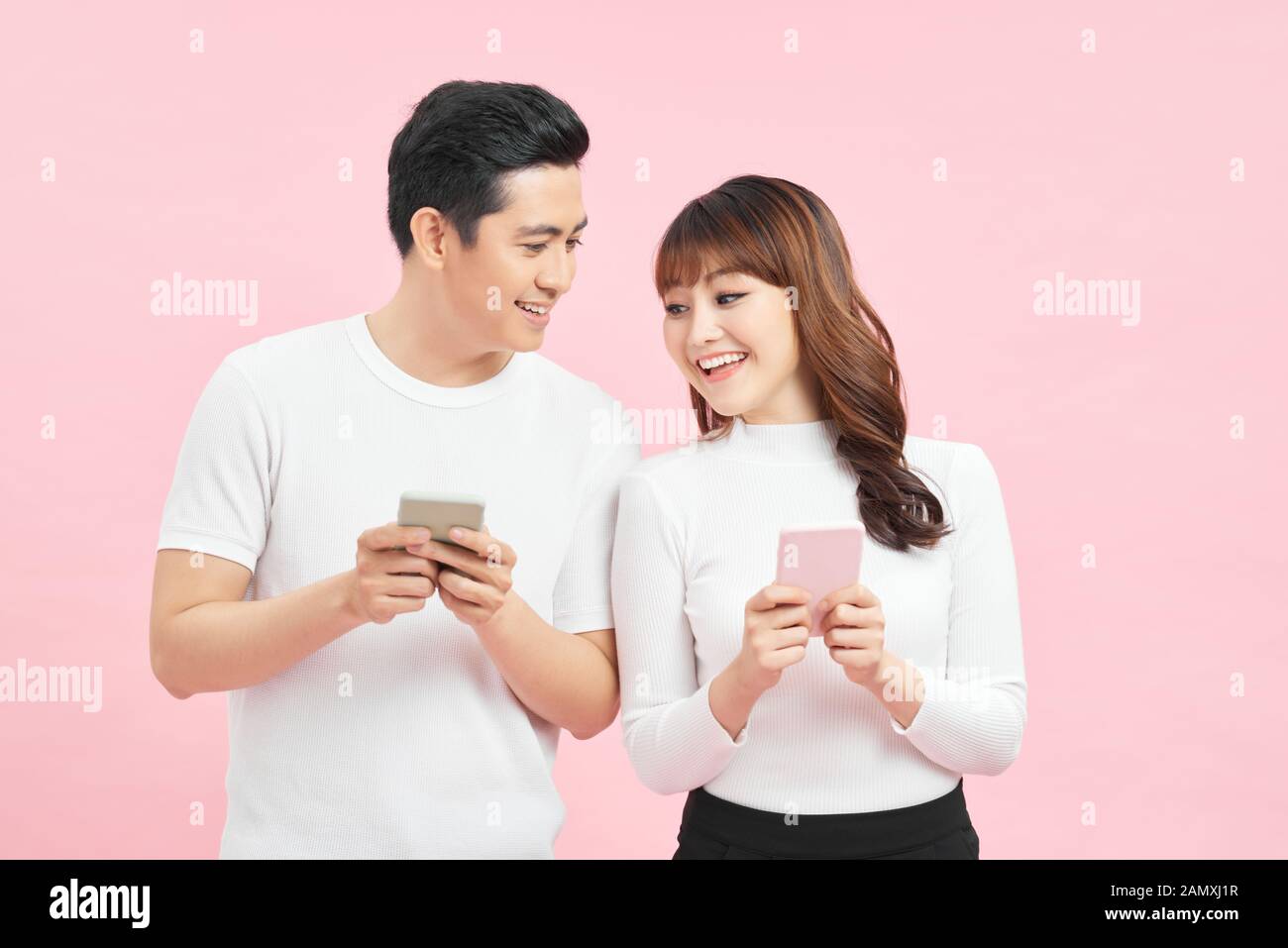 Heureux enchanté beau couple portant des vêtements décontractés isolés sur fond rose, regardant le téléphone mobile Banque D'Images