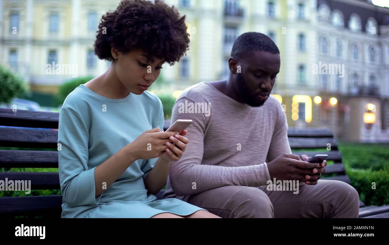 Petite amie et petit ami à discuter dans leurs smartphones, assis sur un banc, ignorer Banque D'Images